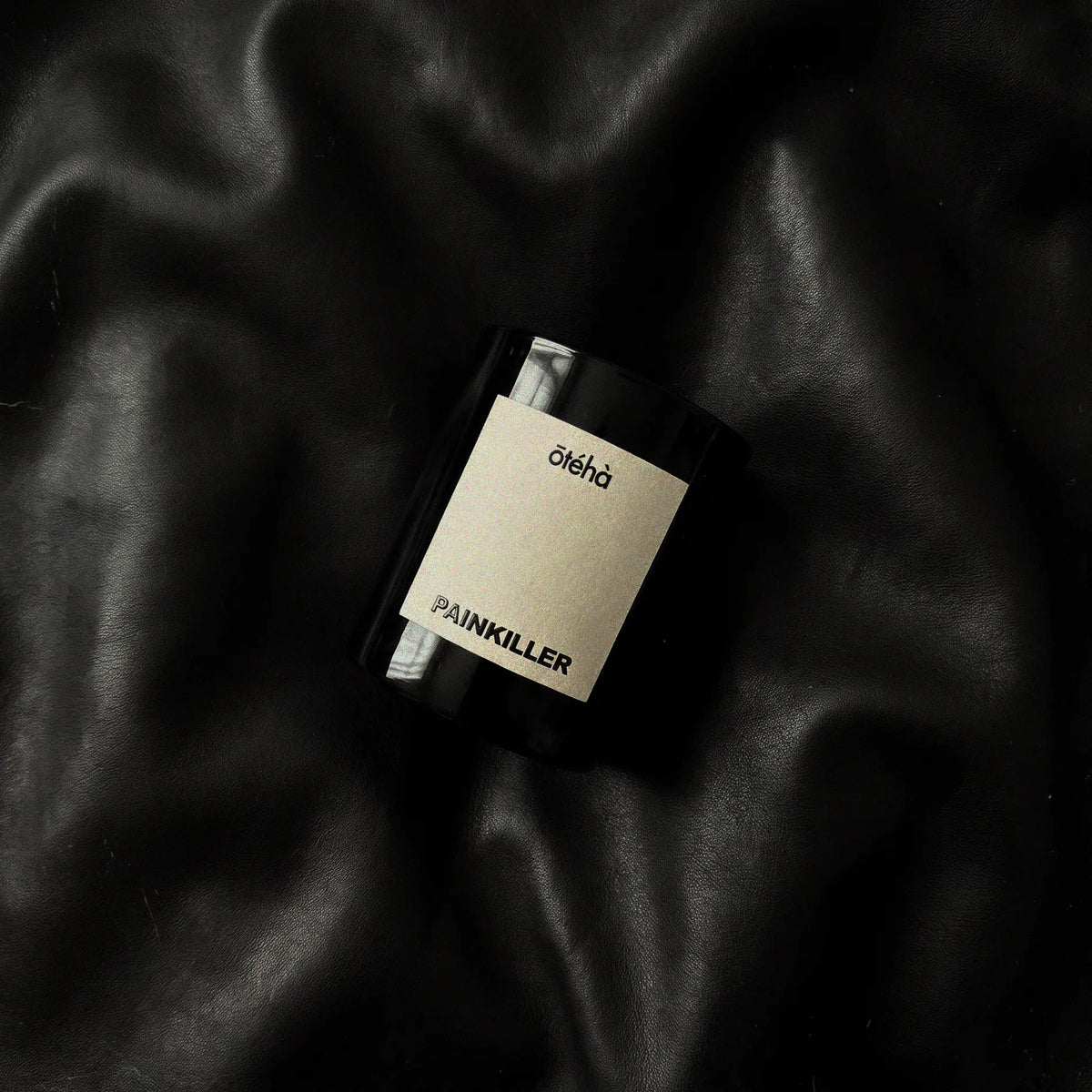 Painkiller scented candle by ōtéhà lying on soft black leather, reflecting its leather scent